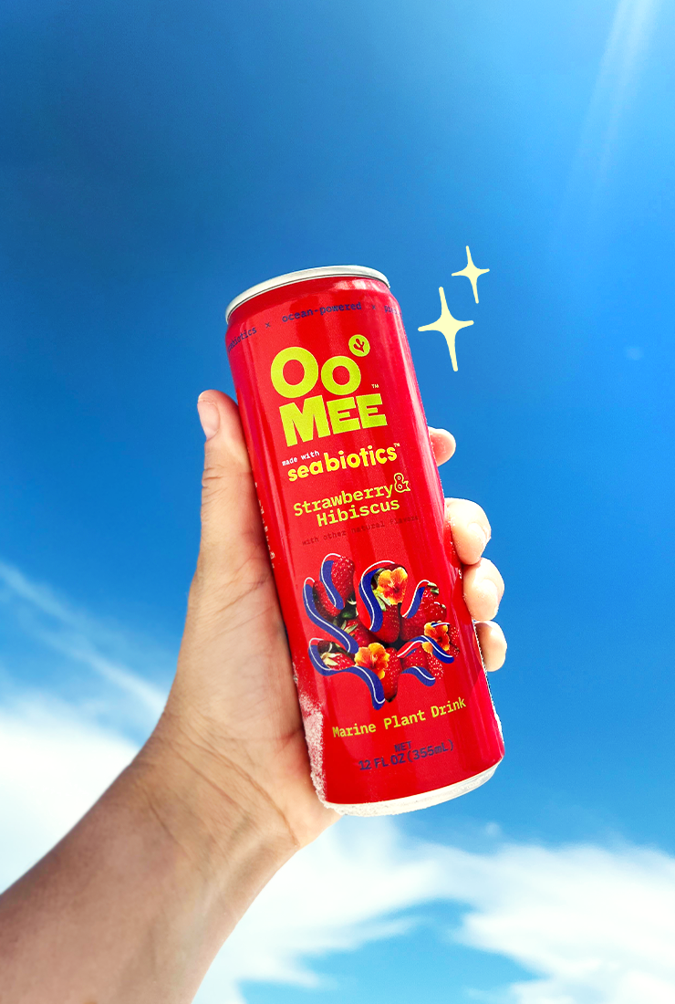 Hand holding a chilled can of OoMee Strawberry & Hibiscus marine plant drink against a bright blue sky, with sparkle accents highlighting its refreshing and vibrant appeal.