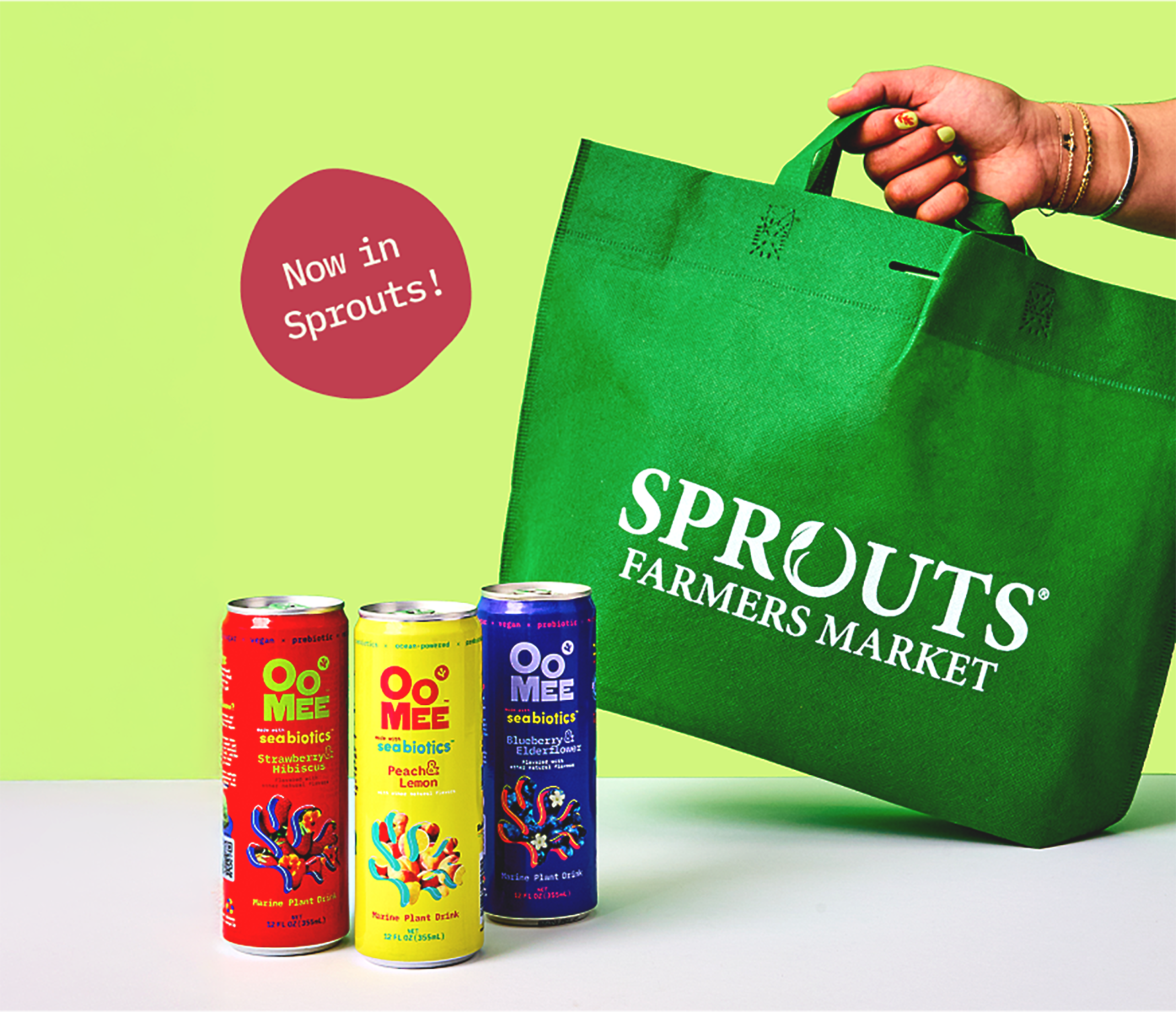 OoMee drinks now sold at Sprouts Farmers Market — three flavors beside a green Sprouts bag.