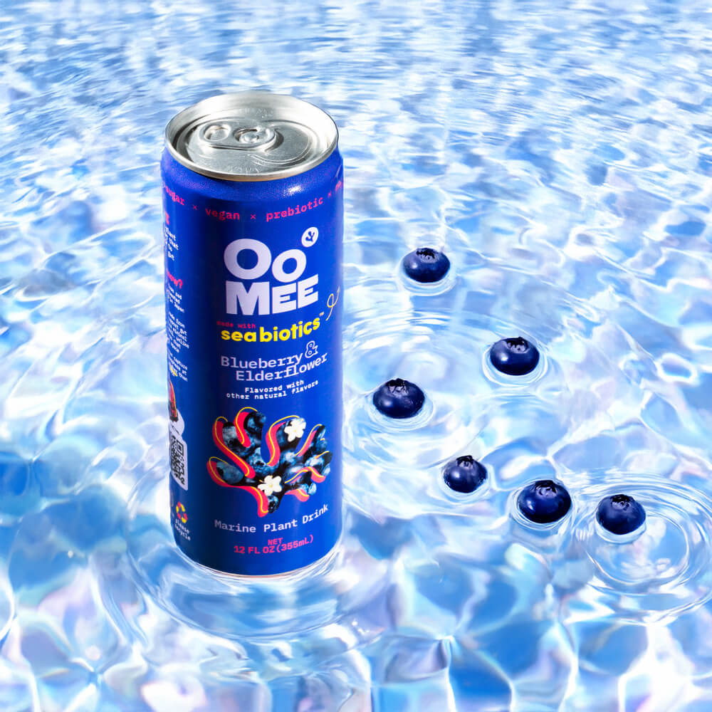 OoMee Blueberry & Elderflower Marine Plant Drink with Seabiotics™ - 12 oz Can Surrounded by Fresh Blueberries Floating in Vibrant Water. Vegan, Prebiotic, Low-Sugar Ready-to-Drink Beverage.