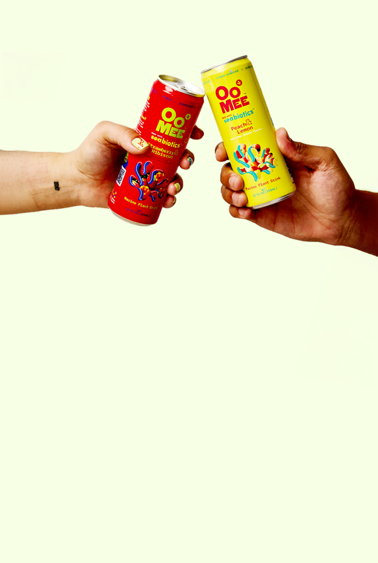 Two hands clinking OoMee marine plant drinks โ one Strawberry & Hibiscus, one Peach & Lemon โ against a light pastel background, symbolizing celebration and refreshment.