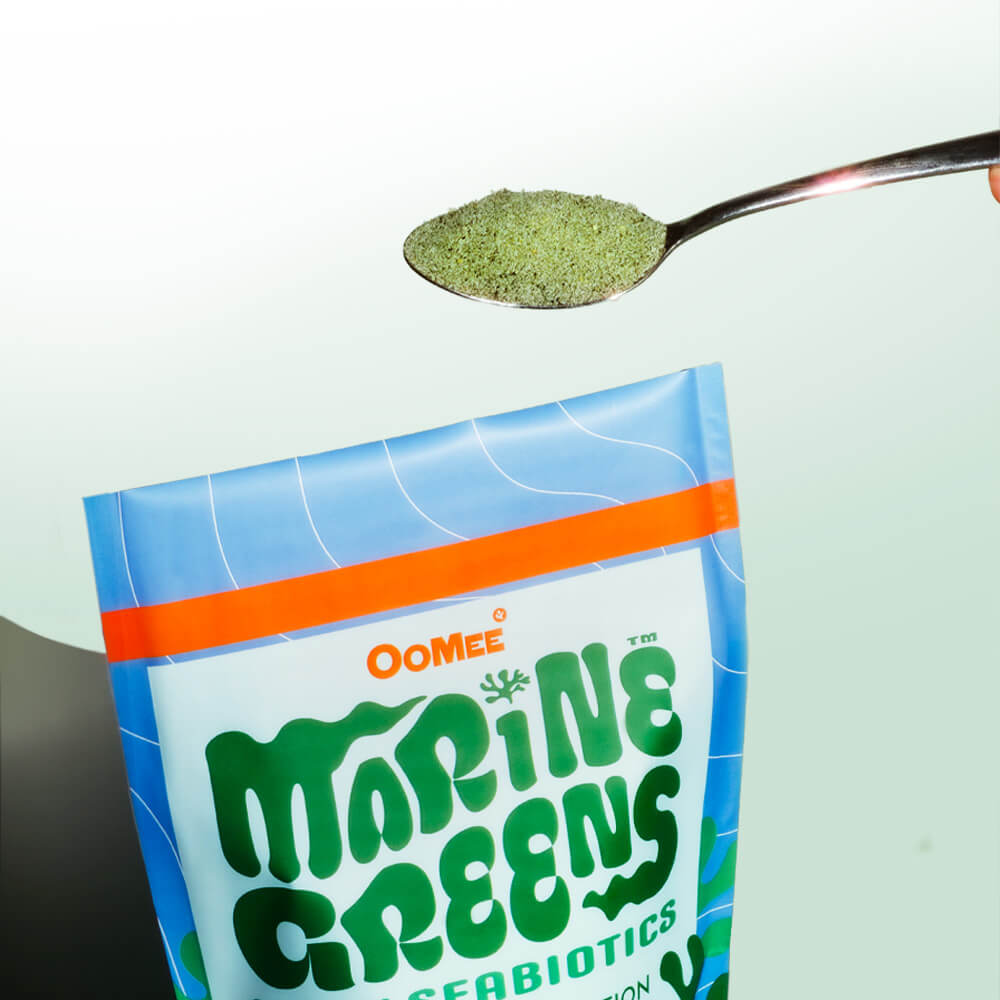 Close-Up of OoMee Marine Greens 30-Serving Stand-Up Pouch with Spoonful of Green Powder Against Light Teal Background - Marine-Based, Green Powder for Gut Health and Nutrition. 