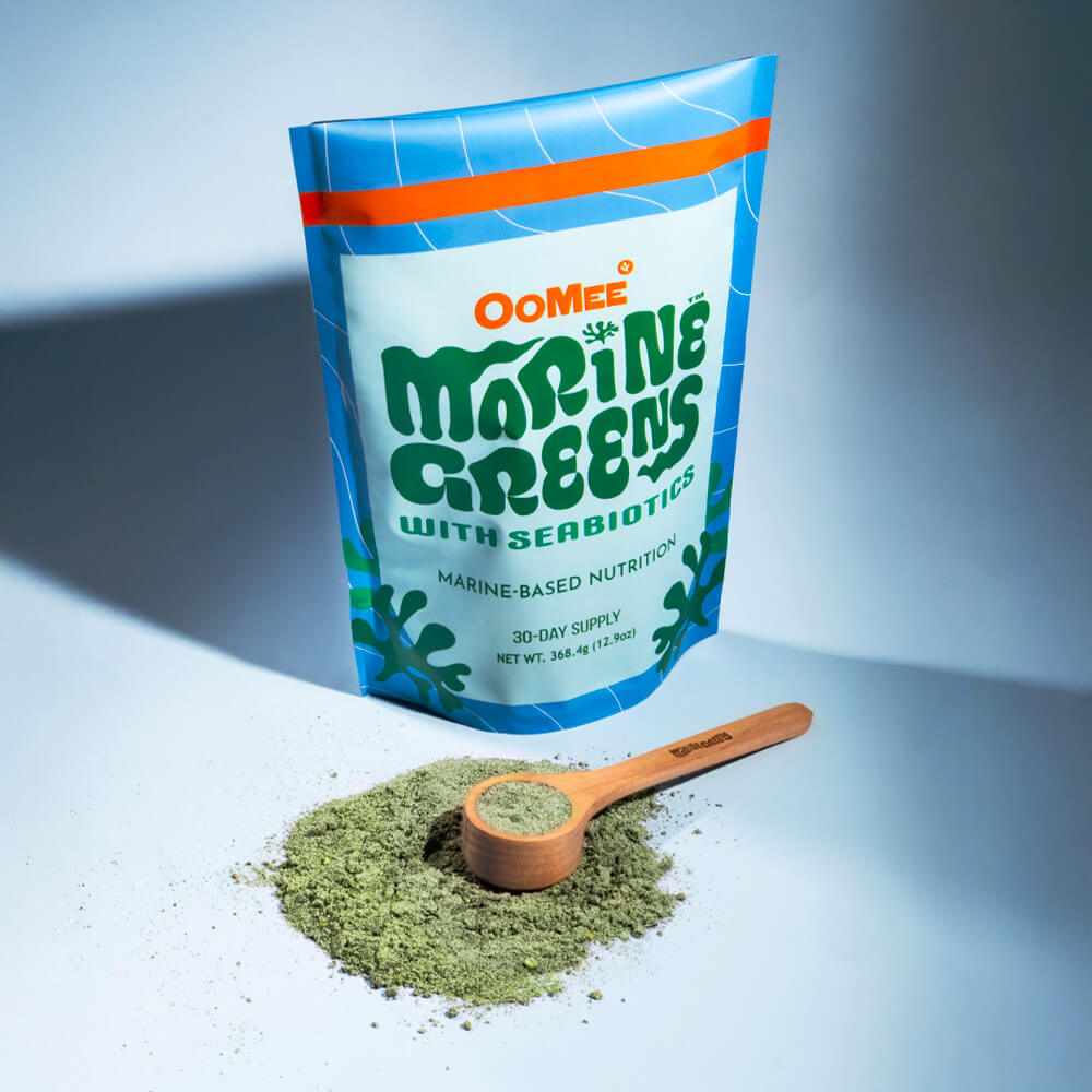 Marine Greens™ 30-serving pouch displayed with a pile of green powder and a free bamboo scooper provided for the first 100 orders. The sleek packaging highlights the marine-based nutrition with Sea-biotics™.